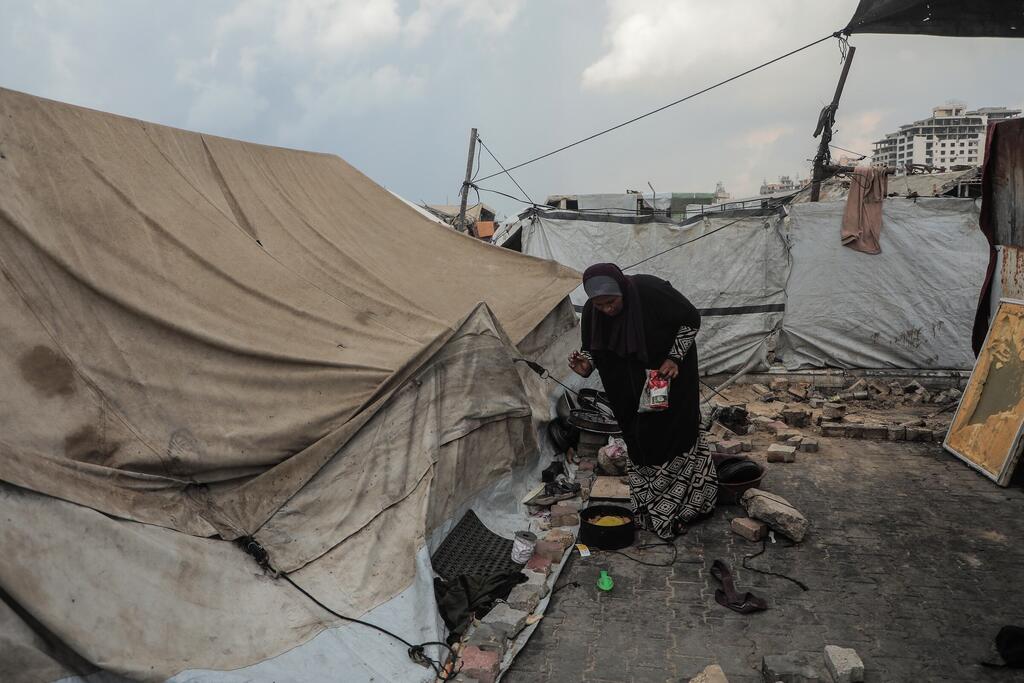 Une mère déplacée à Gaza prépare de la nourriture dans une tente inondée, symbole des terribles conditions de vie des familles touchées par la guerre.